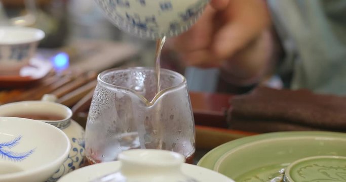 Close up of hands pouring tea from the Gaiwan into the glass pitcher. Gong fu cha session, a traditional chinese tea discipline. High dynamic range professional footage.