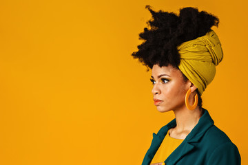 Profile portrait of a serious young woman with big yellow earrings and afro hair wrapped with head wrap scarf