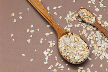 oat flakes in a two wooden spoon on a brown background