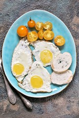  fried eggs and yellow cherry tomatoes. on a blue plate. yellow and blue. top view