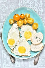  fried eggs and yellow cherry tomatoes. on a blue plate. yellow and blue. top view