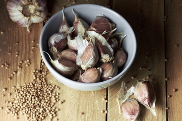 Garlic in a bowl with coriander spice nearby on wooden table, closeup, copy space, dark mood, homegrown food ingredients concept
