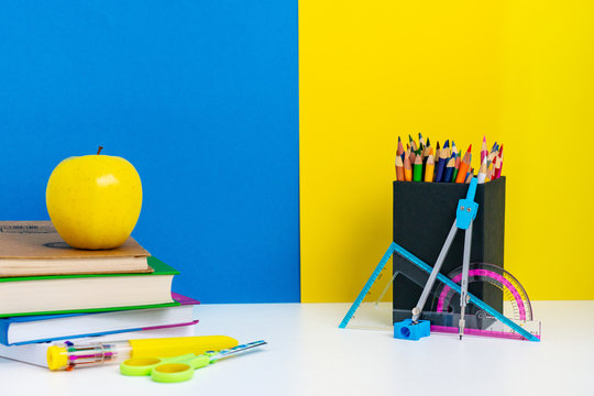 Back to school layout with books, pencils and apple on white table, blue and yellow background, school concept