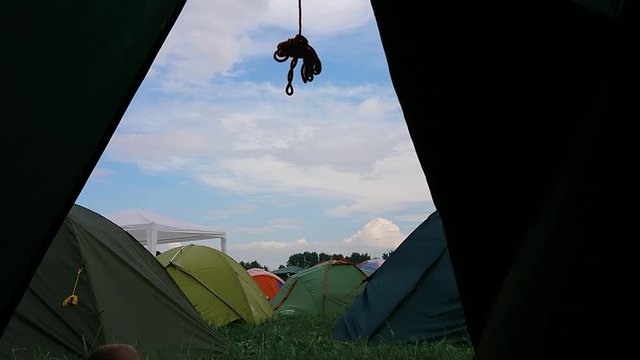 Inside view of the tent on a colorful tent city at a music festival. In the morning, sky, clouds, summer, spring, sun, day, wind, grass, legs, sneakers. Man lies