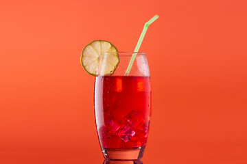 glass of soft drink with a lot of ice a slice of lemon and a straw on orange background