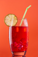 glass of soft drink with a lot of ice a slice of lemon and a straw on orange background
