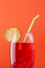 glass of soft drink with a lot of ice a slice of lemon and a straw on orange background
