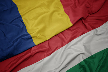 waving colorful flag of hungary and national flag of romania.
