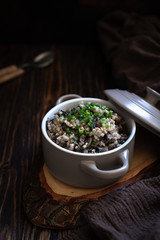 Buckwheat with mushrooms and green onions. A traditional Eastern European side dish or porridge. Healthy vegetarian dish. Served in a ceramic pan on a wooden table. Close-up