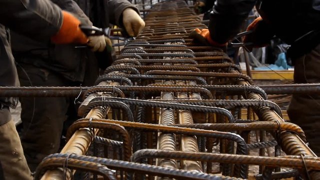 Worker hands use pincers tool and iron wires for knitting metal rods.  Pliers for attaching the rebars to each other. Concrete reinforcement.