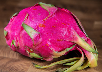 Close up to a red pink dragon fruit on a wooden table. Macro photography of a ripe Pitaya. Wooden...