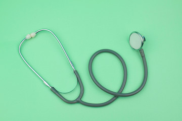 A image of single normal stethoscope isolated on top of a green color paper background