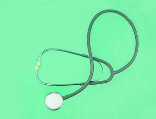 One single normal stethoscope isolated on top of a green color paper background