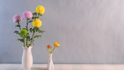 Two white vases with yellow, pink and green dahlias on the table against white wall