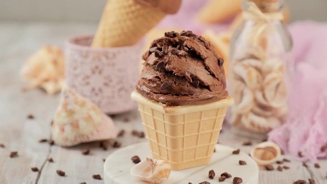 Female hand puts down chocolate ice cream in waffle cone. Summer healthy food concept, lactose free.