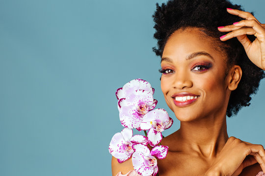 Portrait Of A Beautiful Young Woman Smiling With Pink Make Up, Lips, And Orchid Flower Blooms Around Face