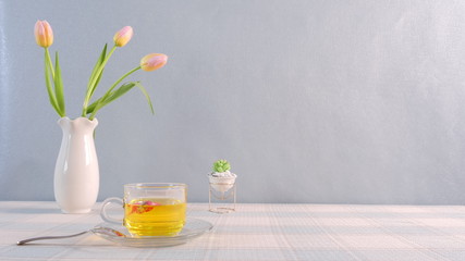 A white vase with pink tulips, a succulent plant and a glass tea cup on table