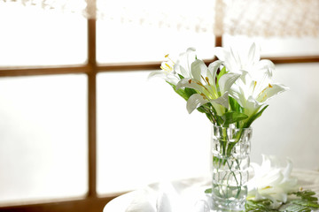 White lily flowers in the vase decorated by the window and bathed in sunlight
