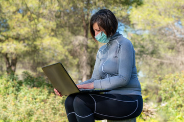 Girl during the coronavirus in a mask at a computer on nature. Social isolation.