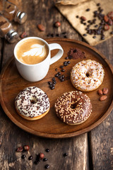 Three donuts and a Cup of coffee on a round wooden tray.
