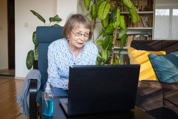 connecting online during coronavirus pandemic elderly woman with laptop chatting in their living room