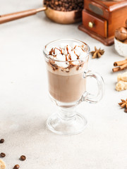 Coffee latte with cream and chocolate topping. On a white table. Next to the coffee beans, vanilla sticks and brown sugar. Space for the text.