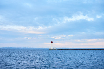 Obraz premium Red and white lighthouse in sea at sunset, copy space. Summer seascape with light house. Black sea