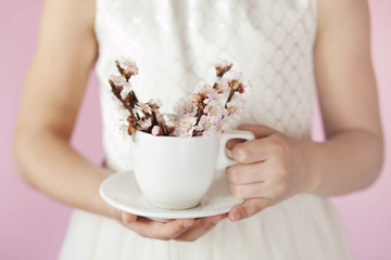 Spring consept. Happy cute child girl with blooming cherry flowers on twigs in a cup in the hands of a young girl indoors.