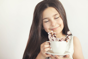 Spring consept. Happy cute child girl with blooming cherry flowers on twigs in a cup in the hands of a young girl indoors.