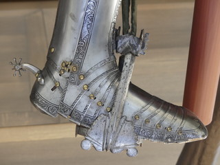 Close up of armored boot with spur on saddle  stirrup . Medieval equipment of armored knight