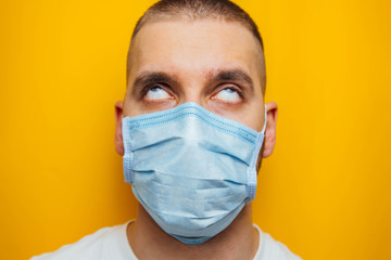 Closeup portrait of an attractive young man rolled his eyes in a protective mask on his face. Fear of getting sick, coronavirus concept. Without pupils.