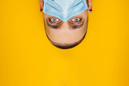 Closeup portrait of an attractive young man rolled his eyes in a protective mask on his face. Fear of getting sick, coronavirus concept. Without pupils.Looks from top to bottom.