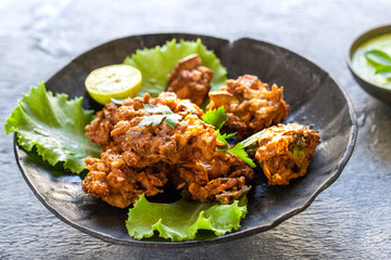 Indian cuisine Indian food. pakora traditional Indian deep-fried snack. pakoras on black plate with coconut chutney sauce curry leaves. national appetiser authentic vegetarian Asian food. travel food