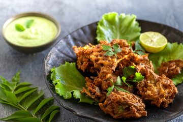 Indian cuisine Indian food. pakora traditional Indian deep-fried snack. pakoras on black plate with coconut chutney sauce curry leaves. national appetiser authentic vegetarian Asian food. travel food.