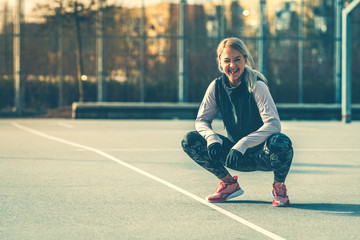 Smiling young Caucasian woman taking a exercises break, squatting and winking