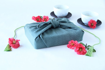 Obraz na płótnie Canvas 赤いボケの花と風呂敷包みと緑茶