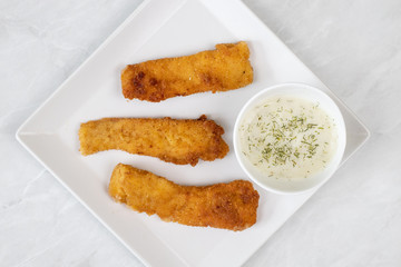 Flat lay above fried chicken meat with dill sauce above white marble background
