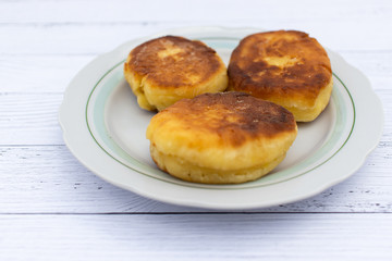 Three fried curd cheesecakes on a white plate on a plank table. Delicious Breakfast of flour, eggs and cottage cheese