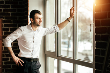 View in profile of a young businessman. Dressed in a white shirt. Standing near the window on a...