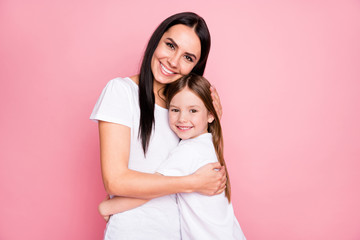Photo of pretty young mommy hold arms hugging little daughter close to herself best friends lovely sincere feelings wear casual t-shirts isolated pastel pink color background