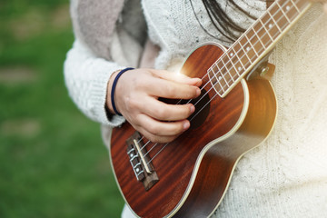 Happy beautiful young woman with pullover fun play acoustic mini guitar ukulele sing a song in...