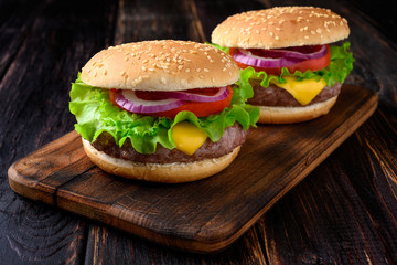 Two burgers on a wooden background. Beef burger with fresh lettuce, tomato and cheese.
