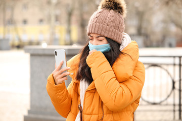 Young Asian woman in protective mask and mobile phone on city street. Concept of epidemic