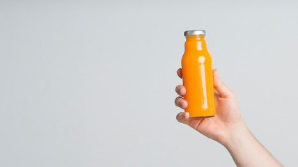 Woman hand with detox orange juice in glass bottle over gray