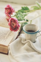 Layout of artificial flowers, a book and a cup with a coffee on a white tablecloth