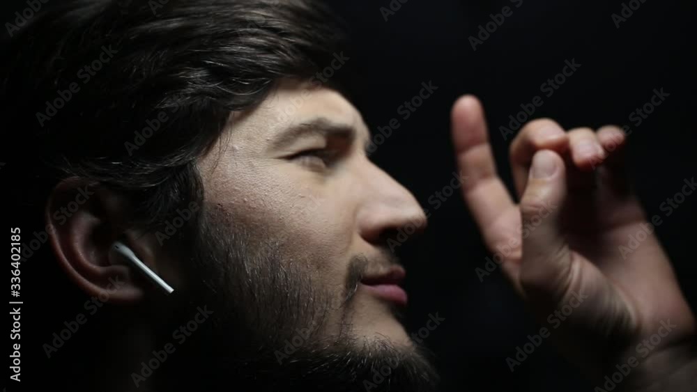 Canvas Prints dark close-up portrait of young man with wireless earphones on black background.