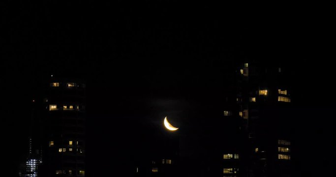 Moon over city. Stunning 4K time lapse of the moon moving slowly over the Sydney city skyline. The moon moves in between two sky scrapers illuminating passing clouds at night.