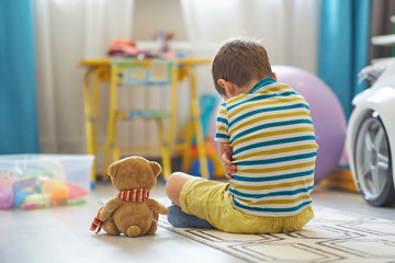 sad boy sits on the floor of the nursery. lonely kid misses home
