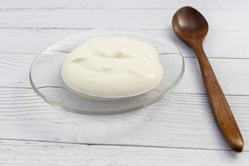 Sour cream, mayonnaise, yogurt on transparent glass saucer and a wooden spoon on wooden white Board