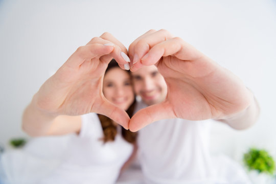 Closeup blurry focus photo of adorable lady handsome guy married couple together overjoyed hold hands making heart figure gesture symbolizing cardiac feelings wear pajama room indoors